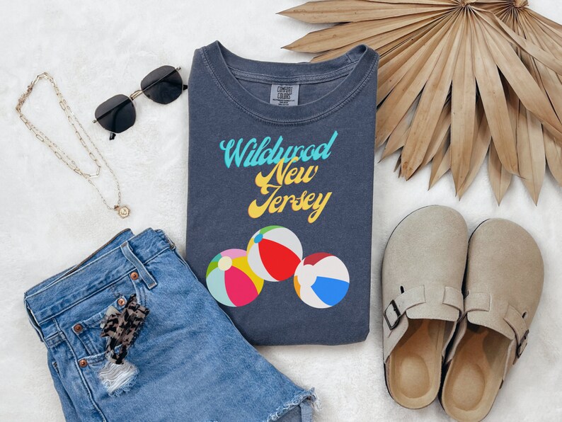 May include: A dark blue t-shirt with the text "Wildwood New Jersey" in yellow and blue lettering. The shirt features three colorful beach balls.