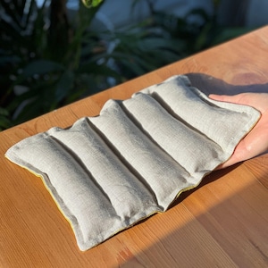 May include: A light gray linen heating pad with a yellow border. The pad is divided into five sections and is designed to be used for warmth or pain relief.