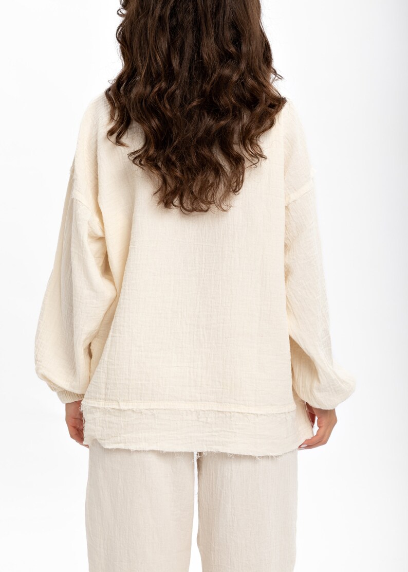 May include: A white cotton lounge set with a long-sleeved top and trousers. The top has a relaxed fit and a slightly frayed hem. The trousers have a straight leg.