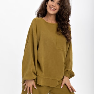 May include: A mustard yellow two-piece lounge set with a long-sleeved top and wide-leg trousers. The top has a relaxed fit and a slightly frayed hem. The trousers have a comfortable, loose fit.