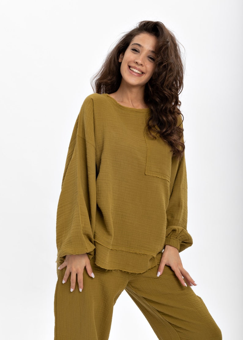 May include: A mustard yellow two-piece lounge set with a long-sleeved top and wide-leg trousers. The top has a relaxed fit and a slightly frayed hem. The trousers have a comfortable, loose fit.
