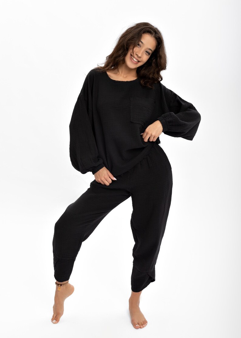 May include: A black two-piece lounge set with a long-sleeved top and trousers. The top has a relaxed fit with a pocket on the left side. The trousers have a wide leg and a relaxed fit.