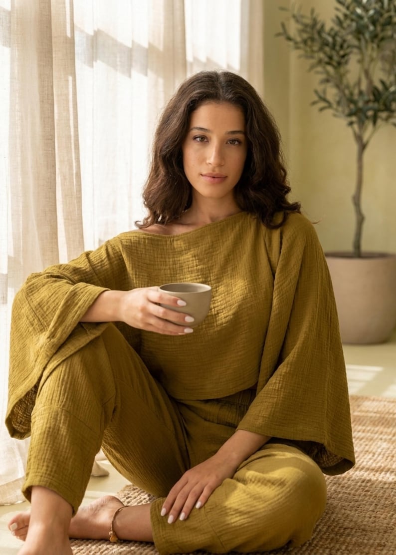 May include: A two-piece lounge set in olive green, featuring a loose-fitting top with wide, flared sleeves and a wide neckline, paired with matching relaxed-fit trousers. The fabric has a visible crinkled texture throughout the entire garment.