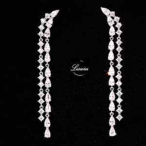 Peut inclure: Une paire de longues boucles d'oreilles pendantes argentées avec plusieurs pierres de zircone cubique claires de forme poire et rondes.
