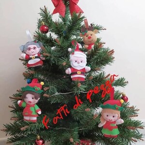 May include: A small artificial Christmas tree decorated with felt ornaments. The ornaments include Santa Claus, a reindeer, a grandmother, and two elves. The tree is decorated with a red bow and the words "fatti di pezzo" are written on the tree.