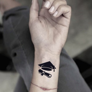 Puede incluir: Un tatuaje temporal negro de un gorro de graduación y un diploma en la muñeca de una persona.