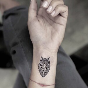May include: A black and white temporary tattoo of an owl with intricate details. The owl is in a tribal style design.