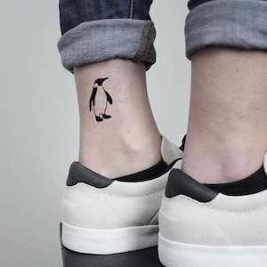 May include: A black silhouette tattoo of a penguin on someone's ankle.