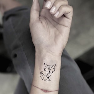 May include: A geometric fox tattoo design in black ink on a person's wrist.