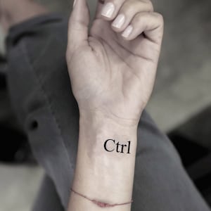 May include: A close-up of a person's wrist with a temporary tattoo that says "Ctrl" in black ink.