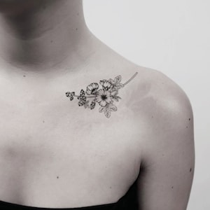 Peut inclure: Un tatouage en noir et blanc représentant un petit bouquet de fleurs sur une branche. Le tatouage est sur l'épaule d'une personne.