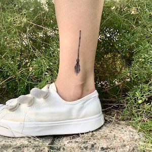 May include: A black temporary tattoo of a witch's broom on a person's ankle.