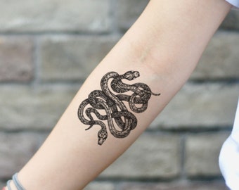 May include: A black and white temporary tattoo featuring two intertwined snakes. The snakes are illustrated in a detailed, vintage style, with scales and intricate patterns. The tattoo is on the forearm.