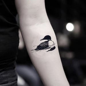May include: A black and white illustration of a loon swimming in water. The loon is facing left and has a long, pointed beak.