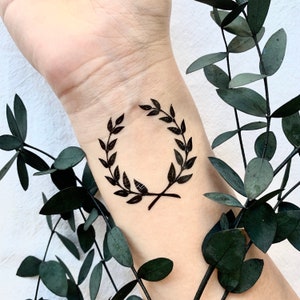 May include: A black temporary tattoo of a simple laurel wreath design on a person's wrist.