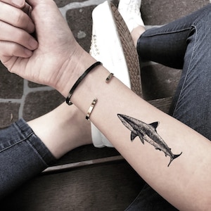 May include: A black and white temporary tattoo of a shark on a person's arm.