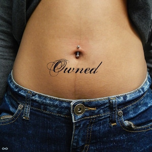 Puede incluir: Primer plano del abdomen de una persona con un piercing en el ombligo y la palabra "Owned" escrita en cursiva debajo.