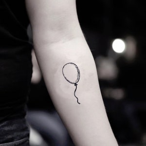 May include: A black, minimalist balloon tattoo on an arm. The balloon is an oval shape with a textured outline and a curved string. The design is simple and elegant, suitable for various styles.
