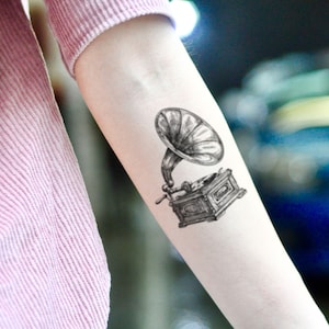 May include: A black and white temporary tattoo of a vintage gramophone with a large horn.