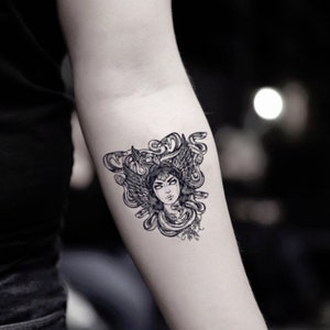 Peut inclure: Tatouage temporaire noir et blanc de Méduse, une figure mythologique grecque avec des serpents pour cheveux, des ailes et un visage humain.