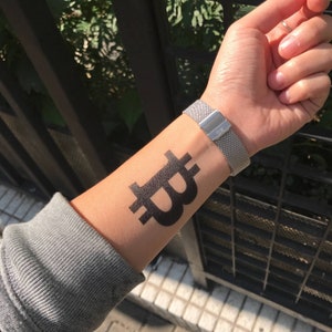 May include: A black Bitcoin symbol temporary tattoo on a person's wrist.