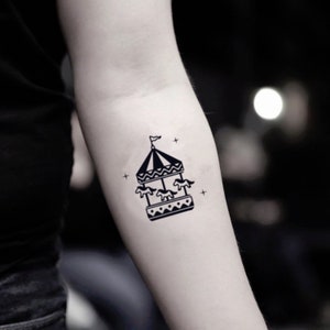 May include: Black and white carousel tattoo design. The tattoo features a carousel with three horses, a striped roof, and a small flag. The design is simple and minimalist, with cross-shaped accents.