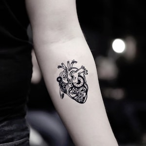 Peut inclure: Un tatouage temporaire noir et blanc d'un cœur humain stylisé avec des engrenages et un mécanisme d'horlogerie à l'intérieur.