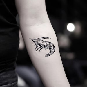 May include: A black and white line drawing of a shrimp on a person's arm.