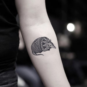 May include: A black and white temporary tattoo of an armadillo. The armadillo is curled up in a ball with its tail tucked under its body.