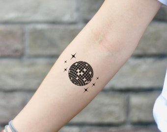 Puede incluir: Tatuaje temporal en blanco y negro con un diseño de bola de discoteca rodeada de estrellas. El tatuaje está aplicado en el antebrazo.