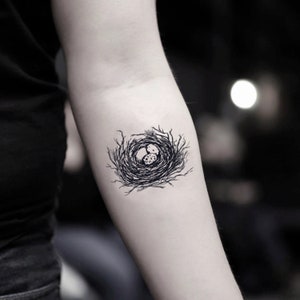Può includere: Un tatuaggio temporaneo in bianco e nero di un nido di uccello con due uova al suo interno.