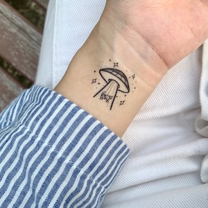 May include: A black and white temporary tattoo of a UFO with stars and a beam of light shining down on a cow.