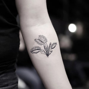 May include: A black and white line drawing tattoo of a Venus flytrap plant.