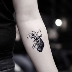 Puede incluir: Tatuaje temporal en blanco y negro de un conejo con cuernos. El tatuaje está en el brazo de una persona.