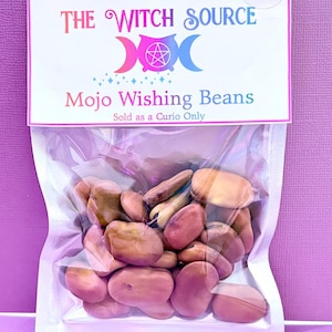 May include: A clear plastic bag filled with brown and pink beans, with a white label at the top. The label reads "THE WITCH SOURCE" above "Mojo Wishing Beans" and "Sold as a Curio Only" in a pink and blue color scheme.