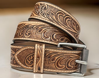May include: A brown leather belt with a detailed floral design and a silver buckle. The belt is folded in thirds, showing the intricate pattern on the leather.