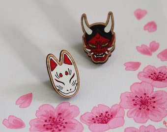 May include: Two wooden Japanese masks, one red and one white, with intricate details. The masks are set against a background of pink cherry blossoms.