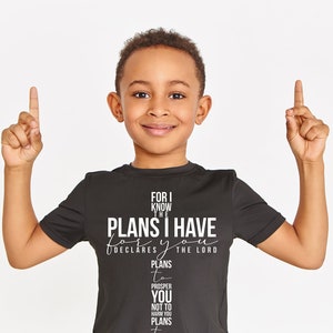 May include: A young boy wearing a black t-shirt with a white graphic that reads "For I know the plans I have for you, declares the Lord. Plans to prosper you, not to harm you, plans to give you hope and a future."