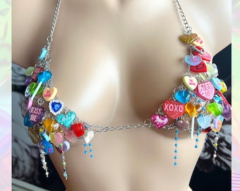 May include: A silver chain body jewelry piece with colorful candy hearts and lollipops attached. The hearts have various sayings on them, including "Kiss Me", "Be Mine", "XOXO", and "Love You".