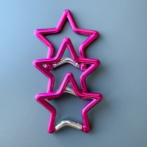 May include: Three pink metal star-shaped keychains stacked on top of each other.