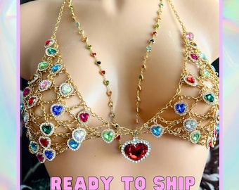 May include: A gold chain body jewellery piece with a large red heart pendant. The chain is decorated with small colourful heart-shaped rhinestones.