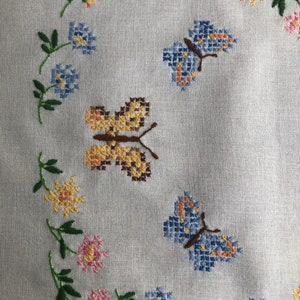 May include: A white linen tablecloth with embroidered butterflies and flowers in shades of blue, yellow, pink, and green.