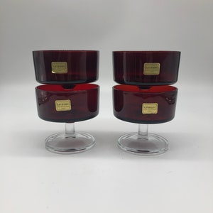 Può includere: Set di quattro bicchieri da vino in vetro rosso con steli e basi trasparenti. Ogni bicchiere ha un'etichetta dorata con la scritta "LUMINARC France".