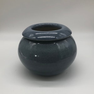 Op de afbeelding: Een kleine, ronde, blauwe keramische pot met een brede, platte rand. De pot heeft een gladde, glanzende afwerking.