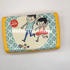 Może przedstawiać: Żółte pudełko na lunch z retro wzorem przedstawiającym dwoje dzieci bawiących się kulkami. Pudełko ma wzór w kolorze niebieskim i zielonym z białymi kółkami. Na pudełku nadrukowany jest tekst "Retro Speelbox".