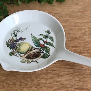 Può includere: Padella da frittura in ceramica bianca con manico. La padella presenta un design botanico con un limone, bacche e foglie.