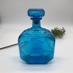 Peut inclure: Une carafe en verre bleu avec un corps carré et un bouchon carré. La carafe a une surface texturée et un motif géométrique.