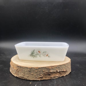 May include: White rectangular baking dish with a floral design featuring white daisies and green leaves. The dish is sitting on a wooden surface.