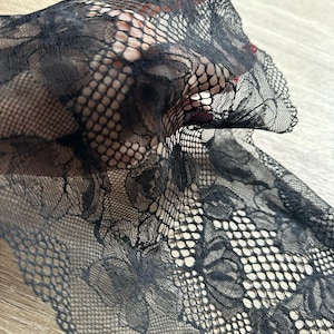 May include: Black lace fabric with a floral pattern. The lace is delicate and intricate, with a fine mesh design.