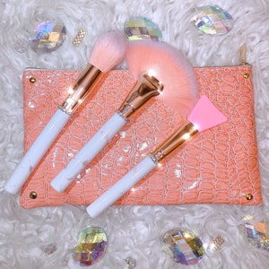 May include: Three makeup brushes with white marble handles and rose gold accents. The brushes are in a pink crocodile-embossed pouch.